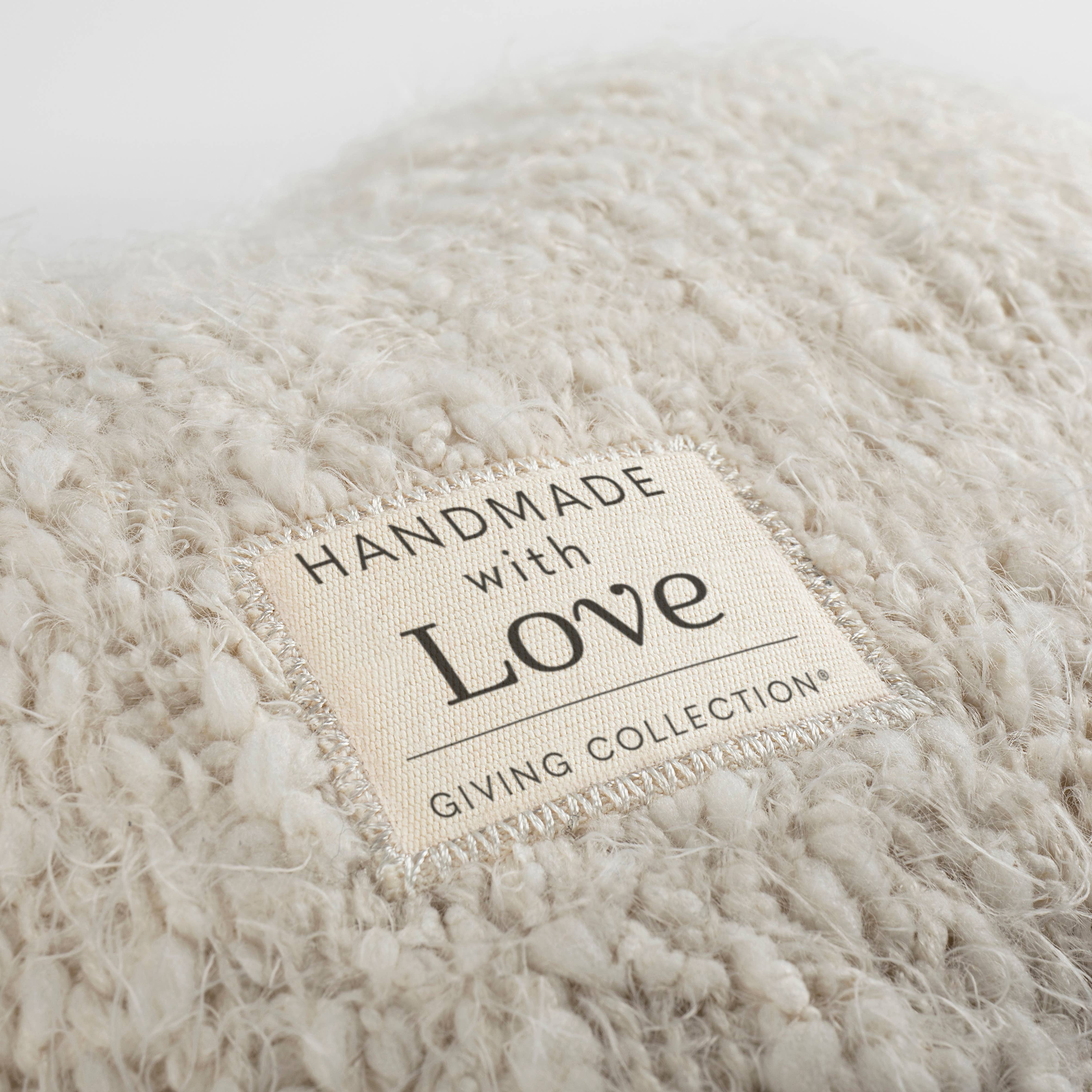 Close-up of the "Handmade with Love — Giving Collection®" woven label sewn onto the cream boucléknit surface of the DEMDACO Giving Heart Weighted Pillow