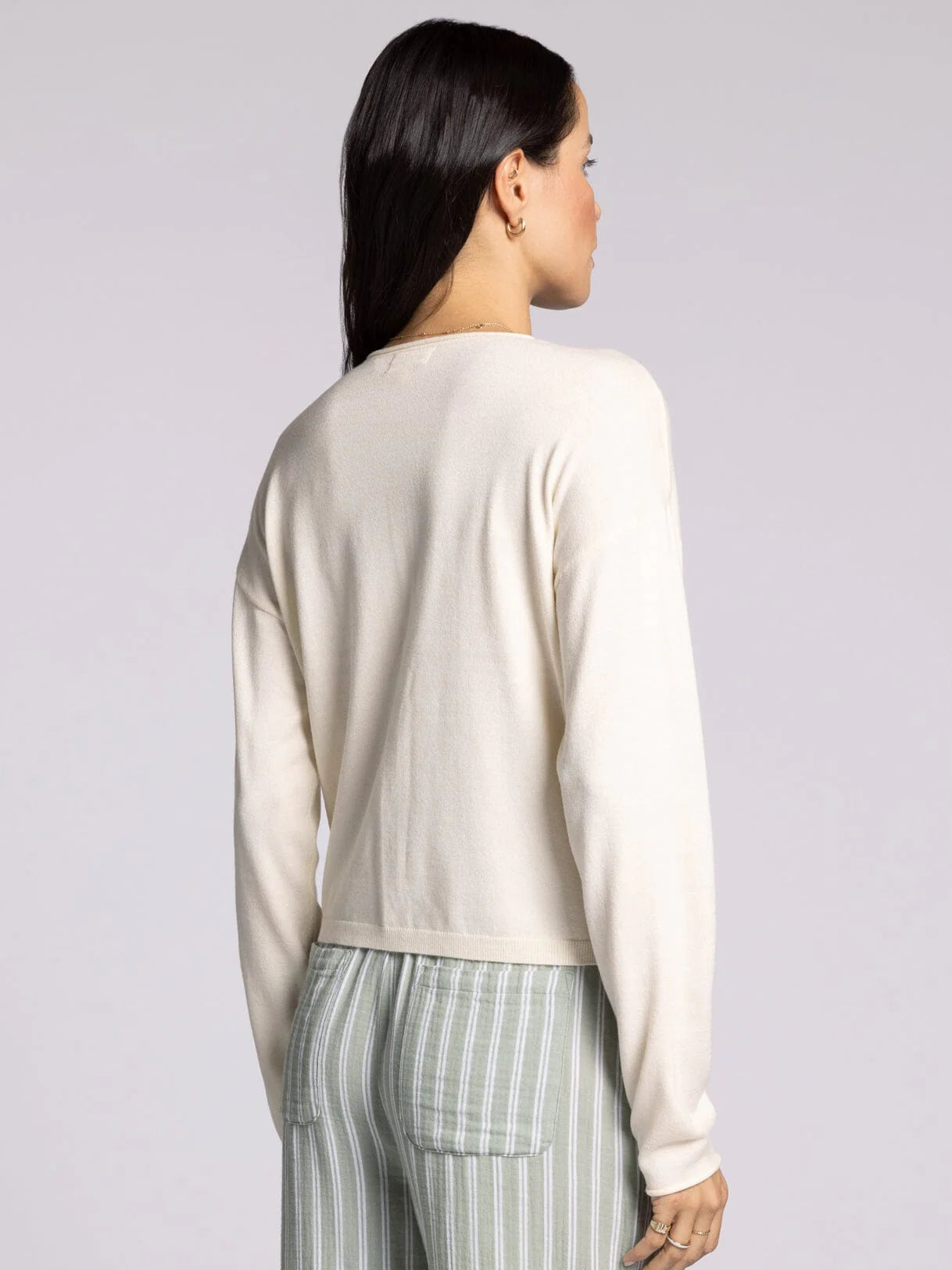 Back view of woman wearing ivory cropped knit cardigan sweater with button front and relaxed fit