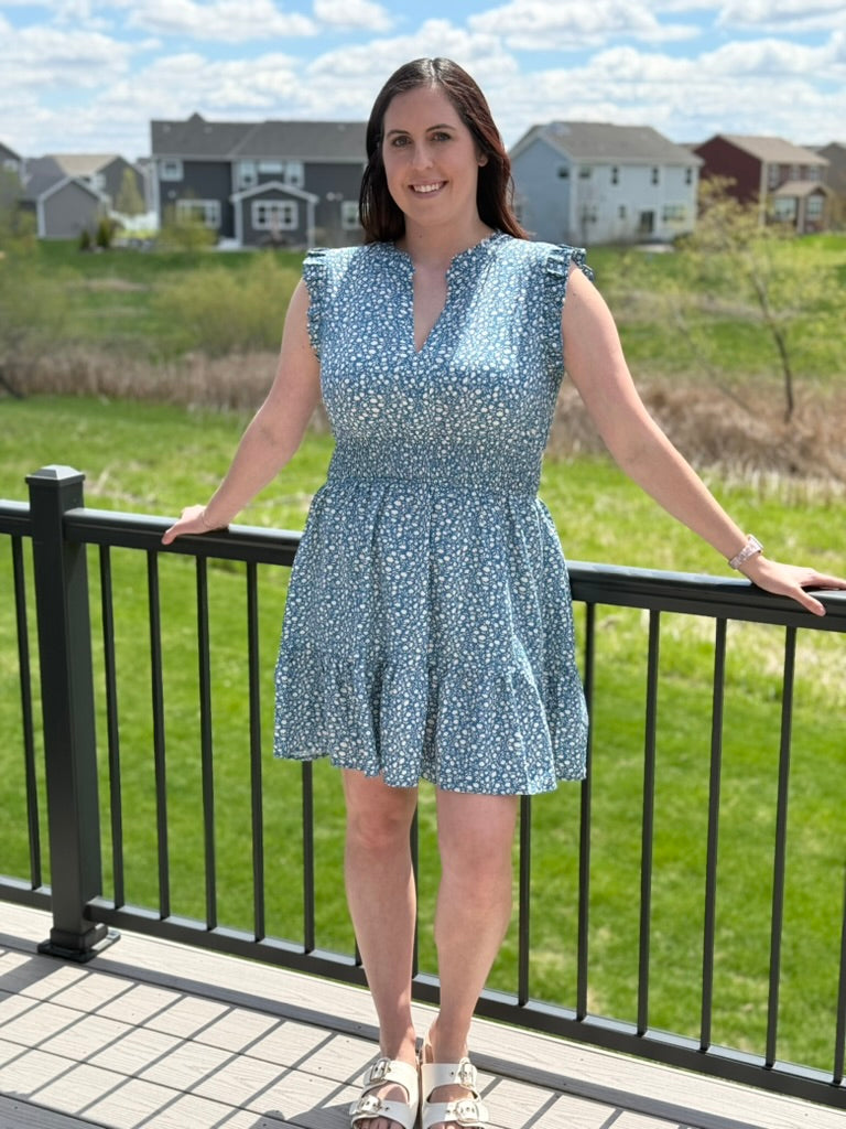 Woman wearing dusty teal ditsy floral mini dress with ruffle cap sleeves and smocked waist
