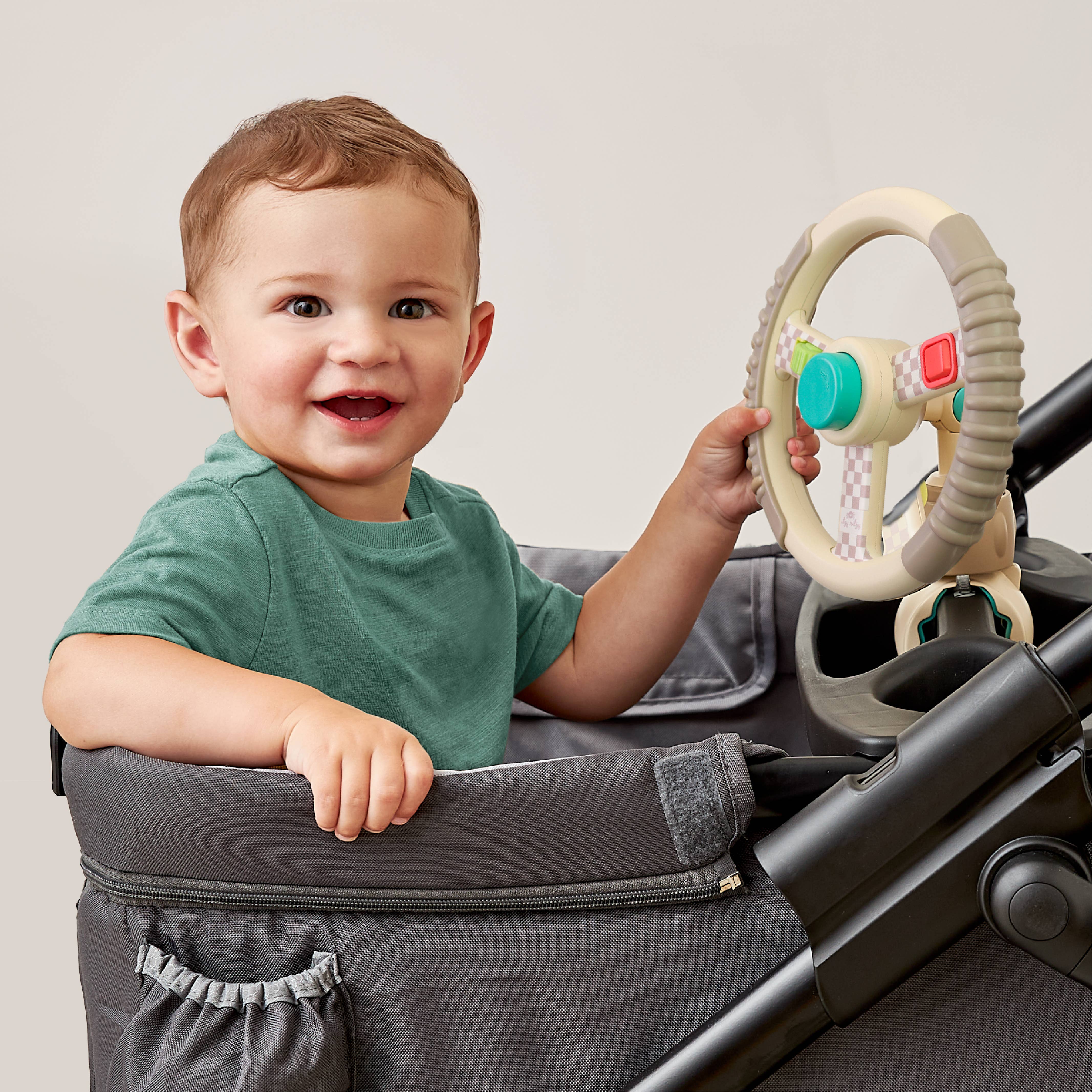 Child playing with bitzy driver in a stroller against a plain background