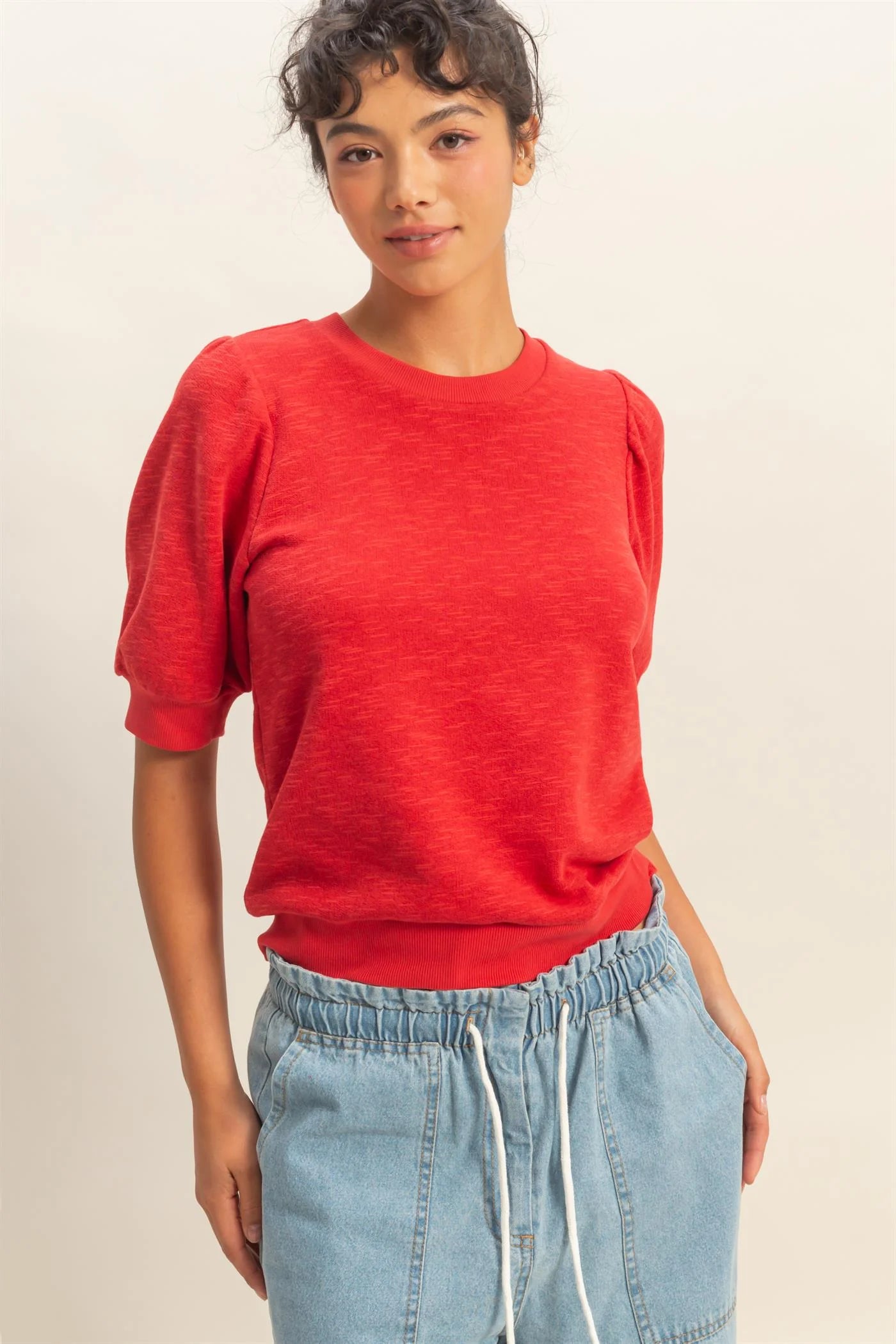woman wearing red puff sleeve crew neck top with stretchy waistband and denim bottoms