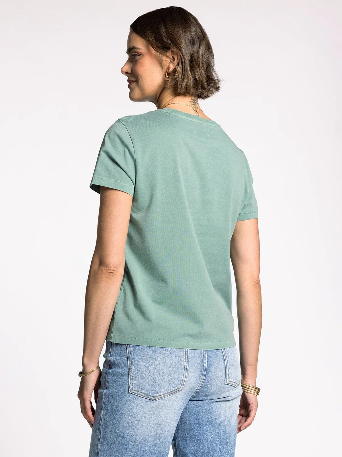 Woman wearing a light green t-shirt and blue jeans on a white background