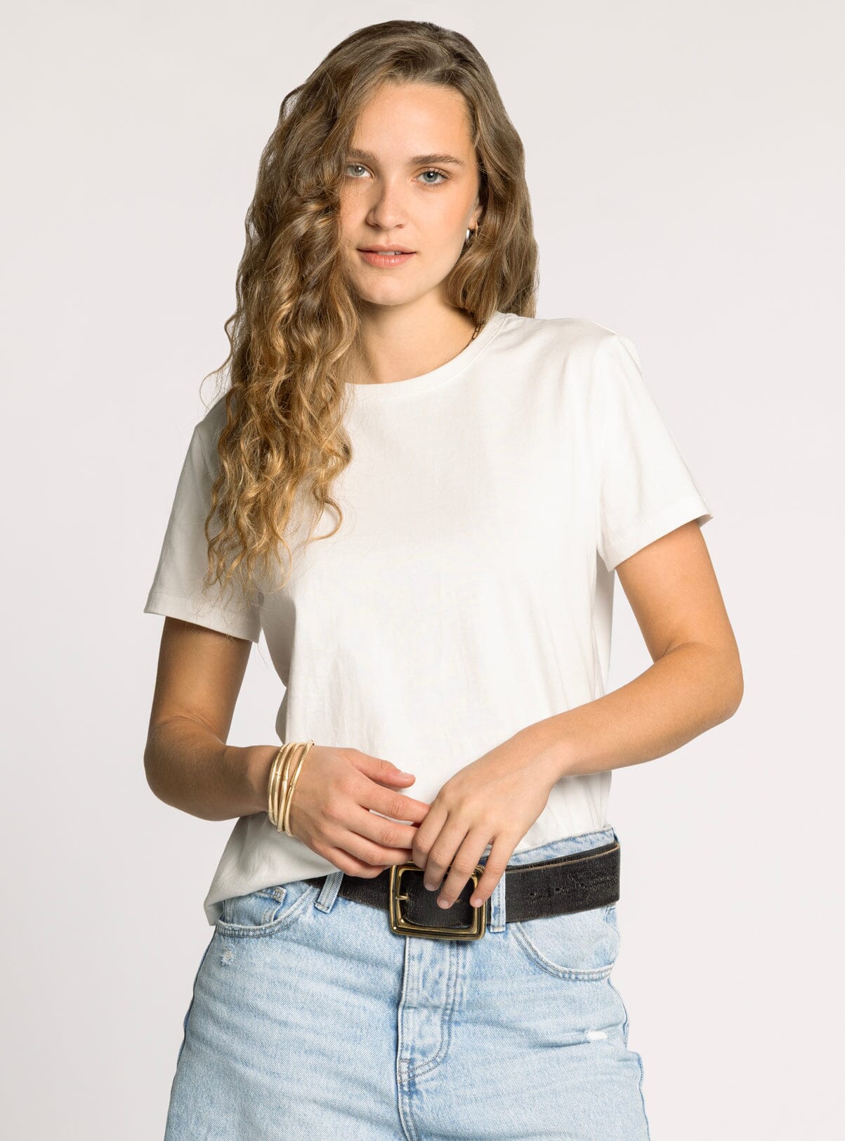 Woman wearing a white t-shirt and light blue jeans against a plain background