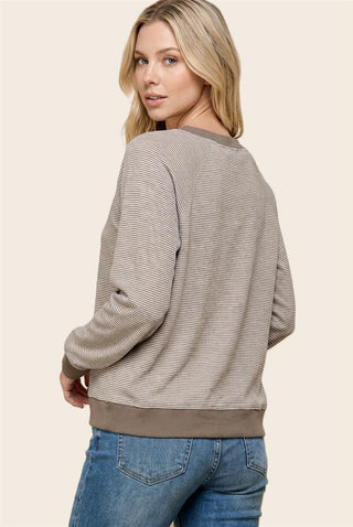 A woman shown from the back wearing a beige and gray striped long-sleeve sweatshirt with solid brown ribbed trim, paired with blue jeans, against a solid light beige background.