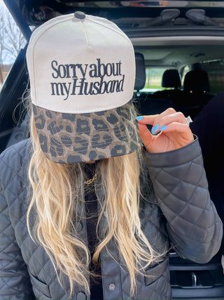 Person wearing a cap with 'Sorry about my Husband' text, standing in a car.