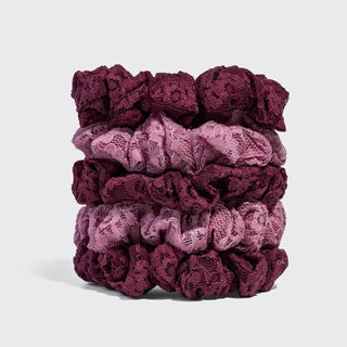 A stack of five lace hair scrunchies in a vertical gradient from deep burgundy to light mauve, photographed on a clean light gray background.