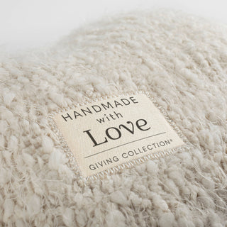 Close-up of the "Handmade with Love — Giving Collection®" woven label sewn onto the cream boucléknit surface of the DEMDACO Giving Heart Weighted Pillow