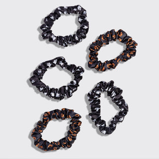 Five black fabric hair scrunchies with Halloween-themed patterns, including orange pumpkins and white skulls, arranged on a light gray background.
