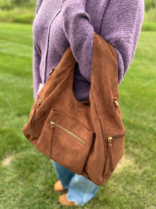 Person holding the Heidi faux suede hobo handbag in the color brown. 
