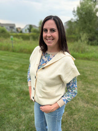 Front view showing button closure and patch pockets, layered over a blue floral long-sleeve top with jeans, outdoors.