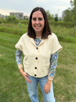 Front view showing button closure and patch pockets, layered over a blue floral long-sleeve top with jeans, outdoors.
