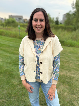 Front view showing button closure and patch pockets, layered over a blue floral long-sleeve top with jeans, outdoors.