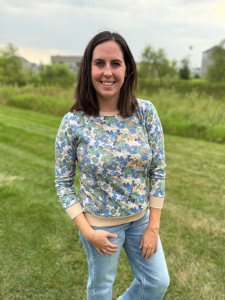 A woman wearing a long-sleeve crewneck shirt with a blue, green, and beige floral pattern, paired with light blue jeans.