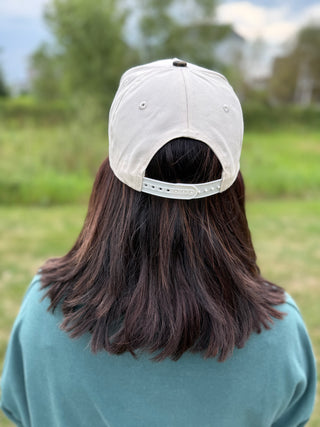 A person viewed from behind wearing a 'sorry about my husband' cream baseball cap.