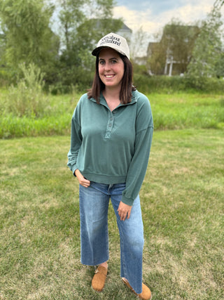 A woman standing outdoors on a grassy lawn wearing a cream baseball cap with leopard print bill with the saying 'sorry about my husband'.