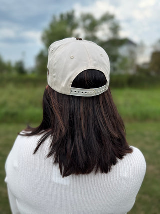 A person viewed from behind wearing a cream baseball cap with the strap adjusted.