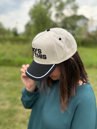 A woman wearing an off white baseball cap with black embroidered text and a black visor.