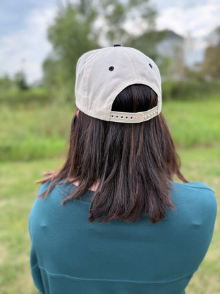 A person viewed from behind wearing an off white baseball cap with a snapback strap.