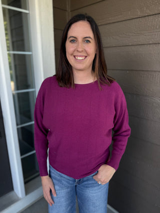 A woman wearing a textured plum long-sleeve knit sweater and blue jeans.