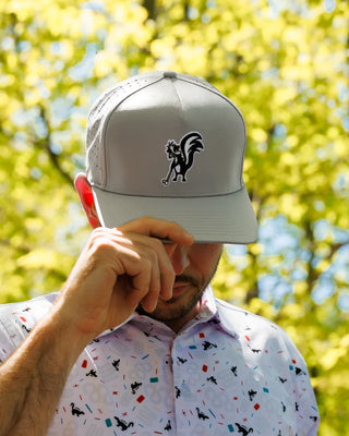 Man wearing Waggle Stinkin' It Up Snapback and matching cribbage print golf polo outdoors — skunk embroidery golf hat lifestyle shot