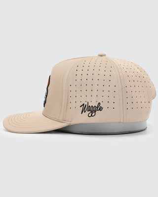 Side view of Waggle Wingman Snapback Hat in tan — fully perforated breathable panels with Waggle script embroidery and grey underbrim
