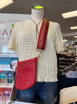 Mannequin wearing a white sweater with a red woven bag in a store setting