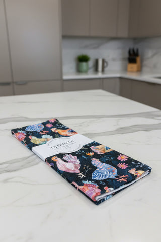 Eco-friendly waffle weave kitchen towel featuring colorful watercolor chickens and wildflowers on a navy blue background.