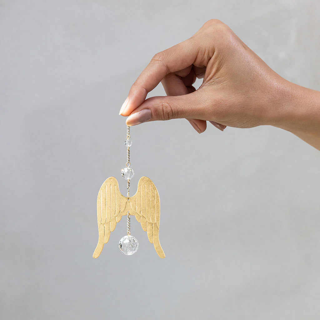 Hand holding Scout Curated Wears Wings Protection mini crystal suncatcher featuring angel wing design with crystal prism and rainbow reflections
