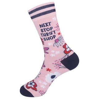 A single pink crew sock with navy blue stripes at the top, the text 'NEXT STOP THRIFT SHOP' in navy blue, and a floral pattern in red, white, and pink, finished with a dark navy heel and toe.