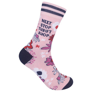 A single pink crew sock with a floral pattern, featuring the text 'NEXT STOP THRIFT SHOP' in navy blue, a navy heel, and a navy toe cap, set against a plain white background.