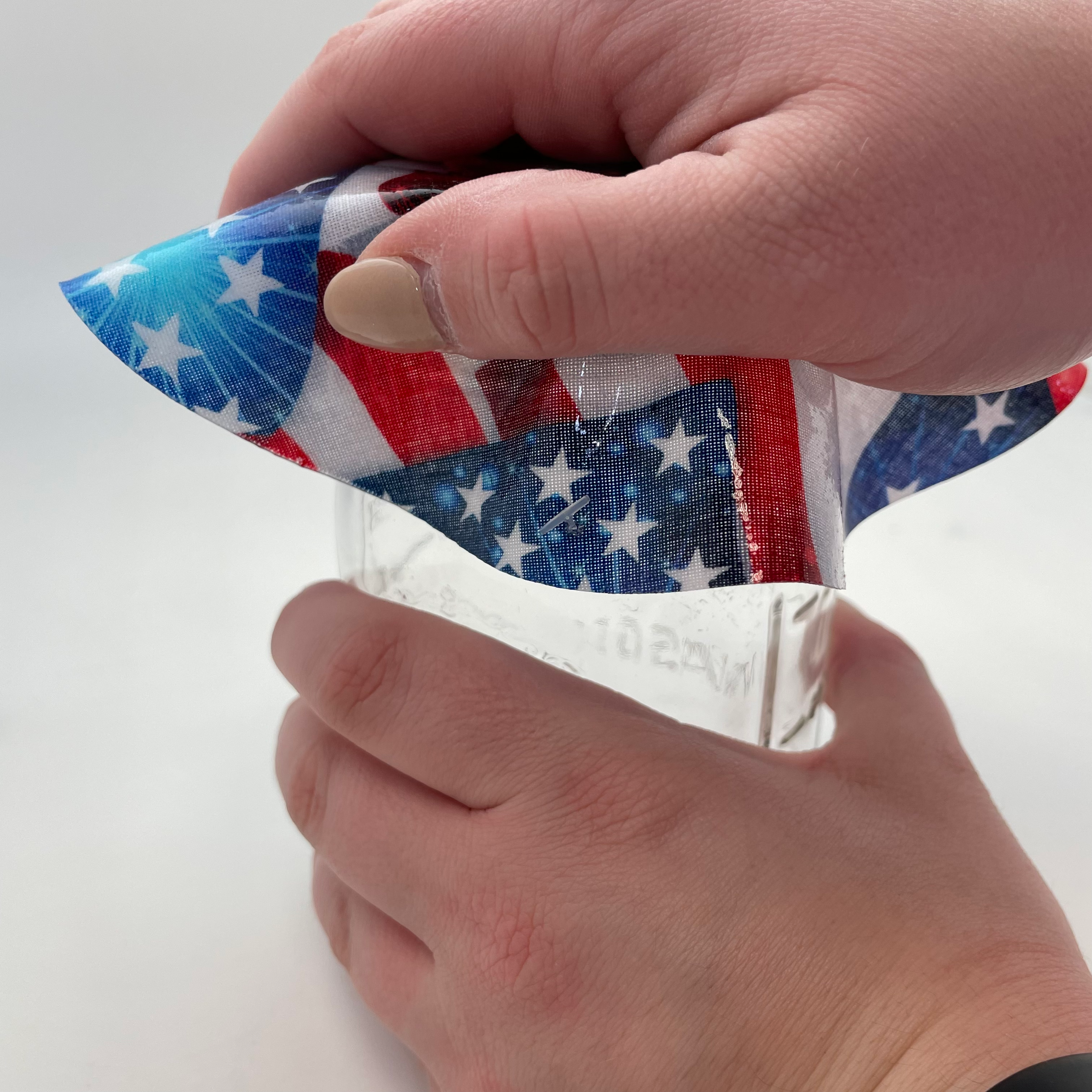 Hand holding an American flag-themed jar opener on a white background