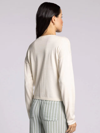 Back view of woman wearing ivory cropped knit cardigan sweater with button front and relaxed fit