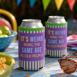 Two funny purple and green can sleeves holding canned drinks at an outdoor party, featuring the saying It’s weird being the same age as old people.