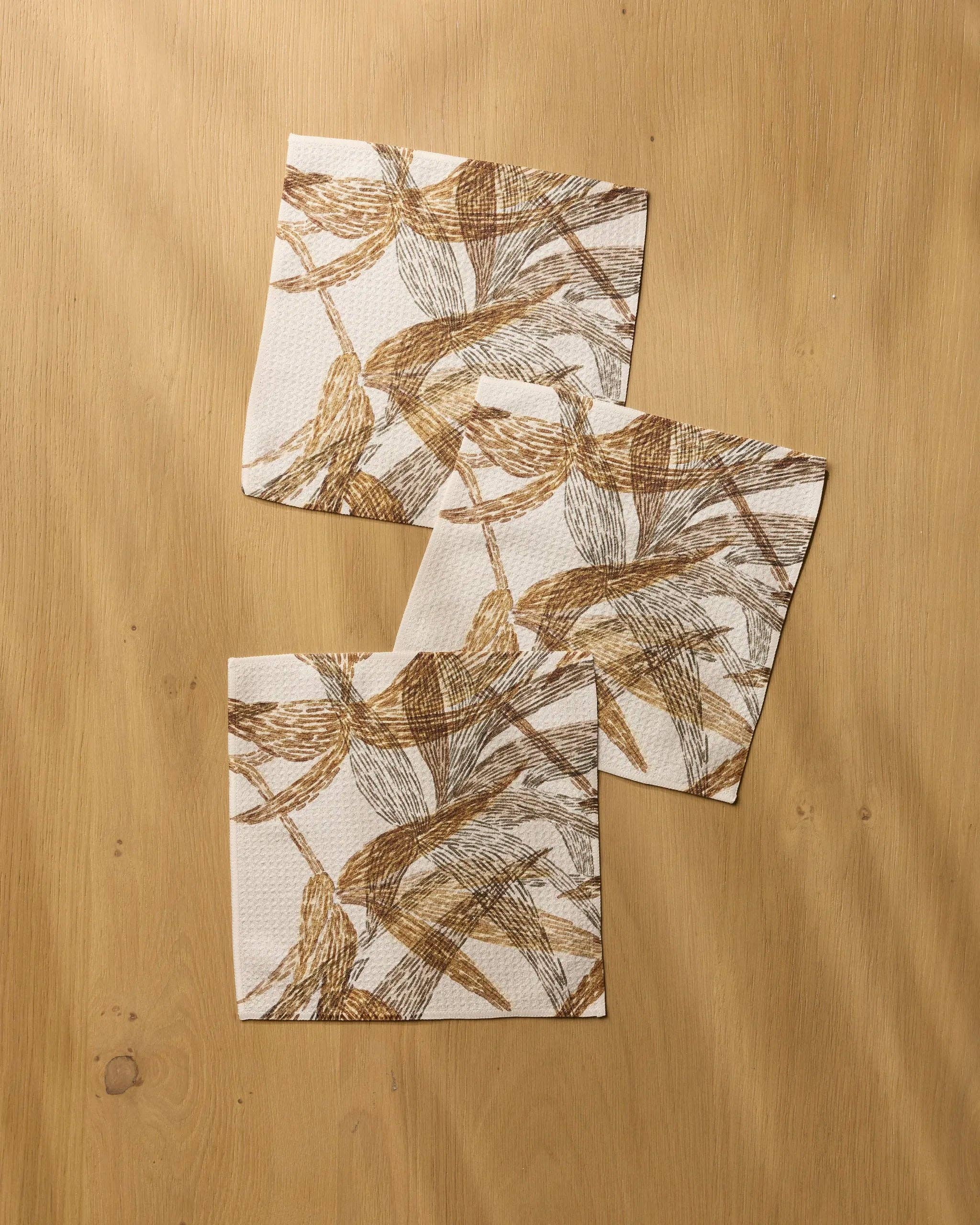 Geometry Amber Wildflower Dishcloth Set 3-pack — warm off-white Geoweave™ dishcloths with stylized brown and dark gray brushstroke leaf print, 10x10 inches each, made from recycled materials
