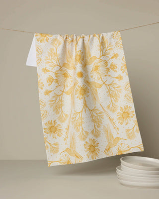 Geometry Gilded Nectar kitchen tea towel featuring gold hummingbirds and wildflowers on an ivory background with quick-drying Geoweave™ fabric.