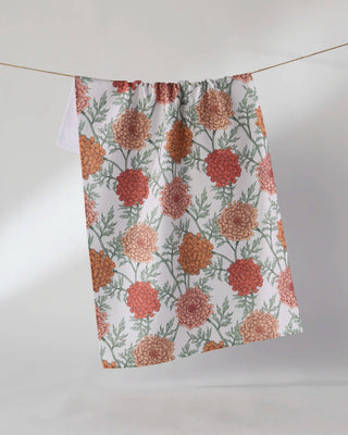 Geometry Marigold Manor Tea Towel hanging on a clothesline showing full 18x30 eco-friendly kitchen towel with warm botanical marigold print in terracotta, burnt orange, and blush on white background