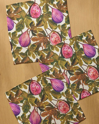 Close-up of Geometry Wild Fig Dishcloth Set 3-pack on wood surface showing detailed botanical fig print with vibrant purple whole figs, pink sliced figs, and earthy green leaves on Geoweave™ recycled fabric