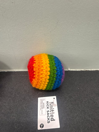 Rainbow-colored knitted kick sack on a gray surface with a label next to it.
