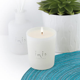 Inis Energy of the Sea Scented Candle lit in frosted white glass on teal woven mat, styled with Inis reed diffuser and succulent plant

