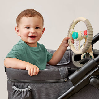 Child playing with bitzy driver in a stroller against a plain background