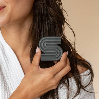 Person holding a gray letter 'S' shampoo bar against a neutral background