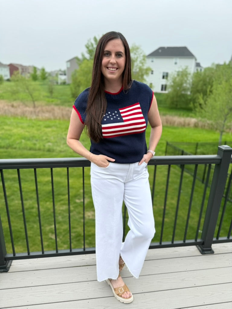 Woman wearing a navy blue t-shirt with an American flag design and white pants standing on a deck.