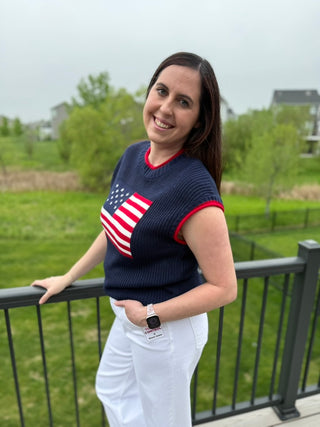 Woman wearing a navy sweater with an American flag design, standing outdoors.