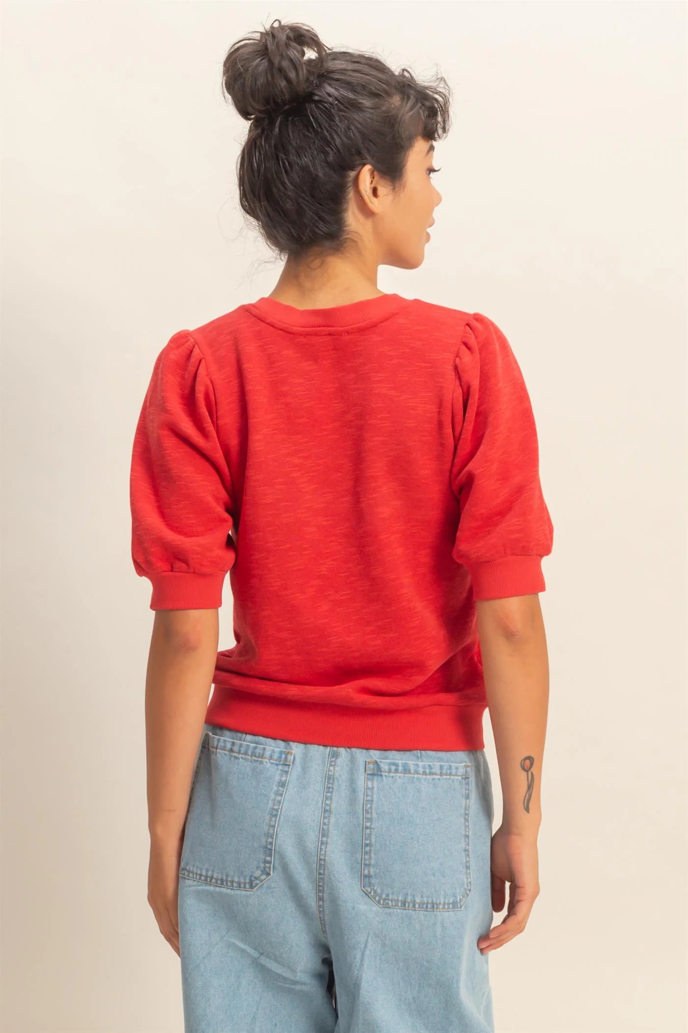 woman wearing red puff sleeve crew neck top with stretchy waistband and denim bottoms back view