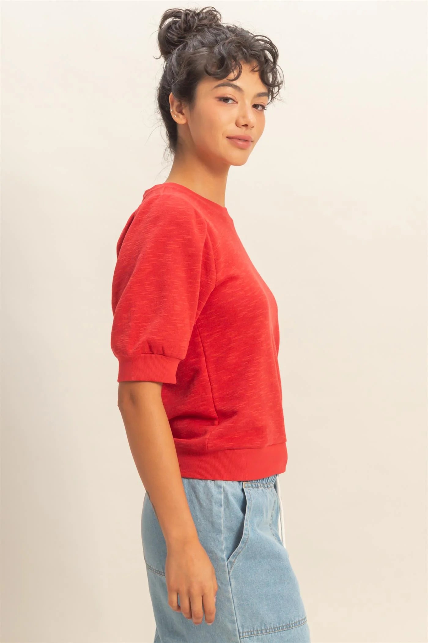woman wearing red puff sleeve crew neck top with stretchy waistband and denim bottoms side view