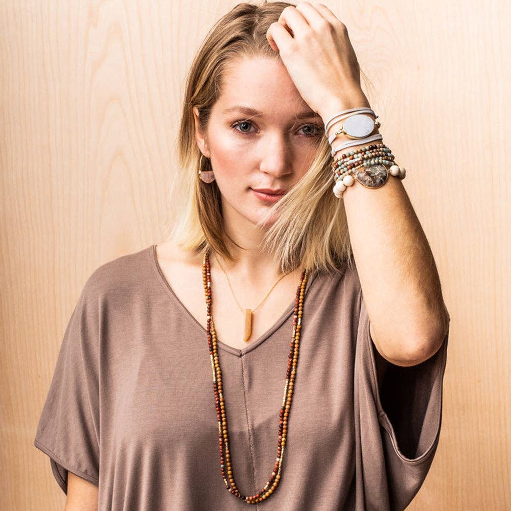 Woman wearing multiple bracelets and a necklace against a wooden background