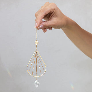 Hand holding Scout Curated Wears Peace Tranquility mini crystal suncatcher featuring gold-plated brass design with crystal prism and rainbow reflections