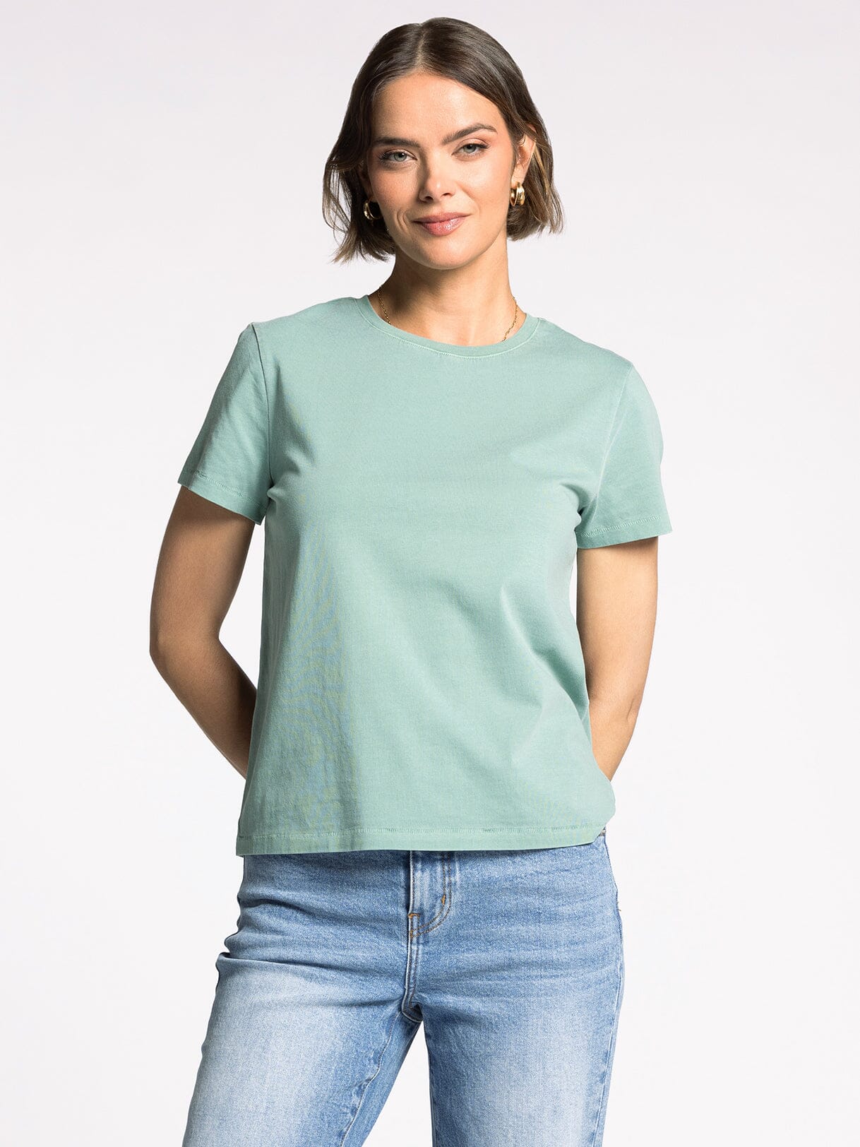 Woman wearing a light green t-shirt and blue jeans on a white background