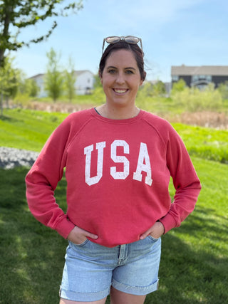 Woman wearing red USA patriotic graphic sweatshirt with distressed white lettering